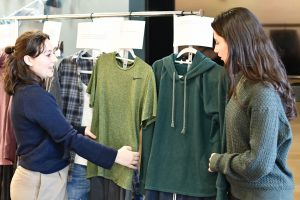 Two students prepare clothing on hangers at an exhibit.