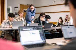Professor Green points to something on a student's computer while others work at tables in the room.