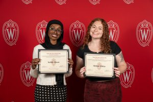 Two women pose with their certificates in front of a red backdrop.